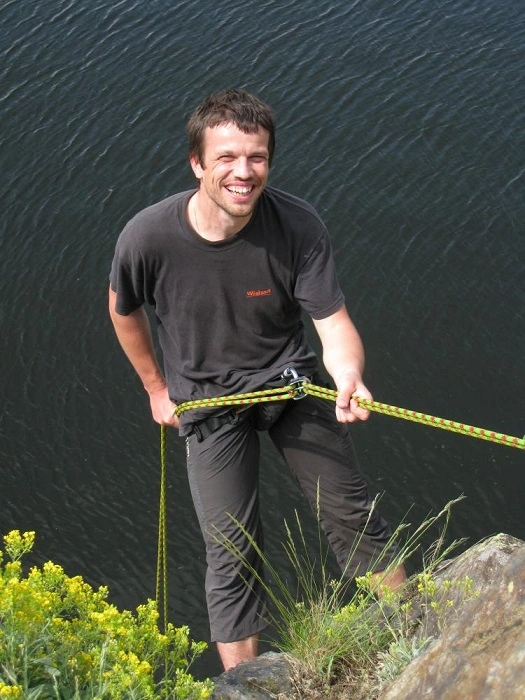 Geocacher ATIP při lezení na skalní stěně během hledání adrenalinové T5 keše u vody.