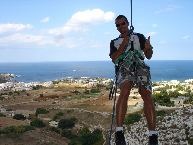 Geokačer během lezení po skalní stěně při odlovu T5 keše s výhledem na moře – adrenalin a dobrodružství v geocachingu.