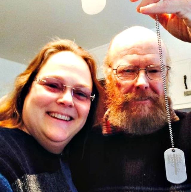 Usmívající se pár drží vojenskou identifikační známku nalezenou při geocachingu – příběh ztraceného a znovu nalezeného pokladu.