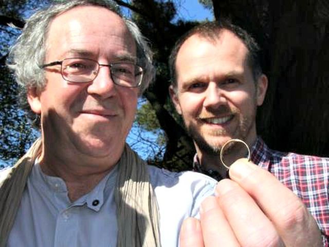 Dva muži drží nalezený zlatý snubní prsten – příběh nečekaného nálezu při geocachingu.