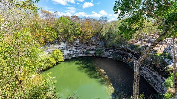 Cenote Sagrado v Chichén Itzá, posvátná studna obklopená skalami a tropickou vegetací.