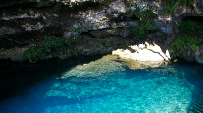 Cenote Yaxbacaltun s tyrkysově modrou vodou a skalními stěnami ukrytá mimo město na Yucatánu.