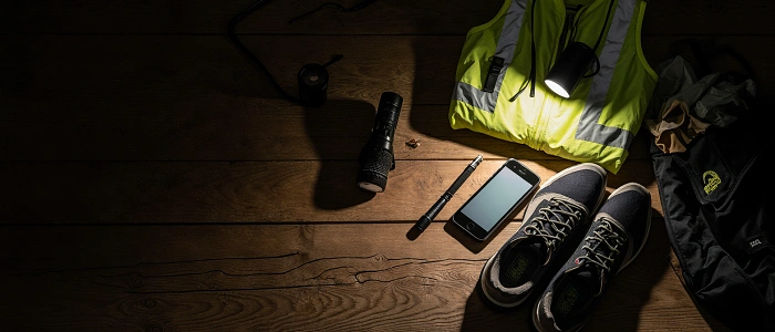 Výbava na noční geocaching – svítilna, reflexní vesta, telefon, boty a batoh připravené na dřevěném stole.