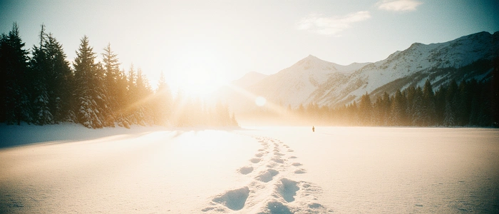 Stopy ve sněhu vedoucí zimní krajinou směrem k horám při východu slunce – dohledávání kešek podle stop v zasněžené přírodě.