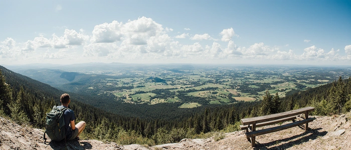 Turista s batohem sedí na vyhlídce s nádherným výhledem do krajiny – chvíle klidu, kdy se geocaching mění v pozorování.