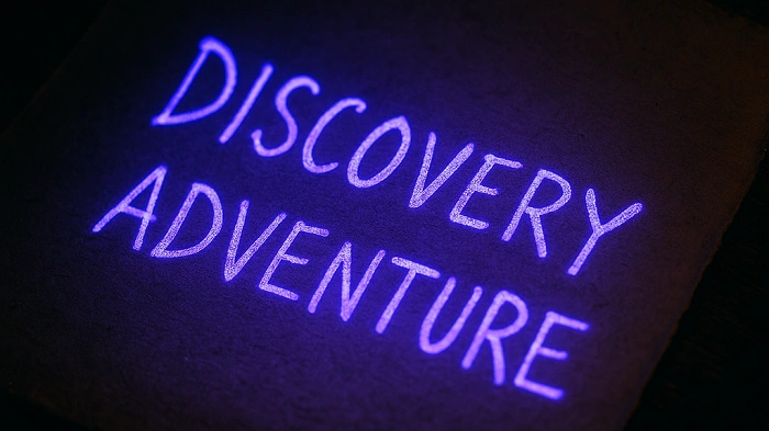Nápis „Discovery Adventure“ svítící pod UV světlem symbolizuje tajemství a objevování speciálních atributů v geocachingu.