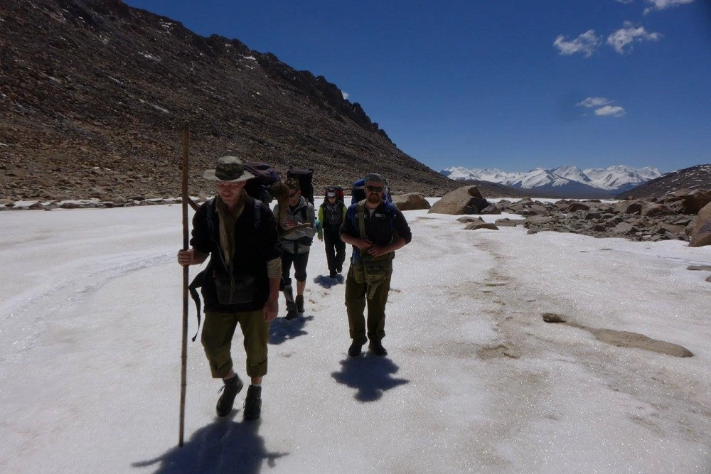 Skupina turistů kráčí po sněhovém poli v kyrgyzských horách směrem k ledovci.