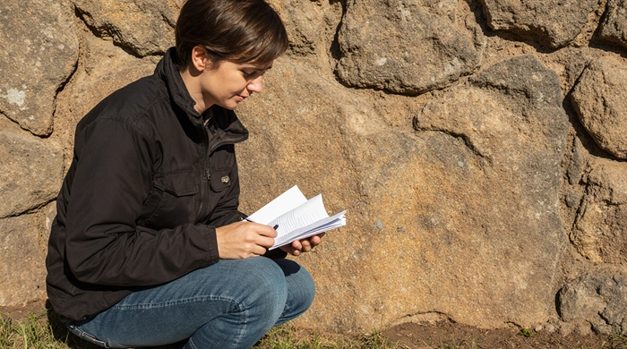 Geokačer zkoumá skálu s GPS v ruce při odlovu Earthcache a zapisuje poznámky o geologickém útvaru.