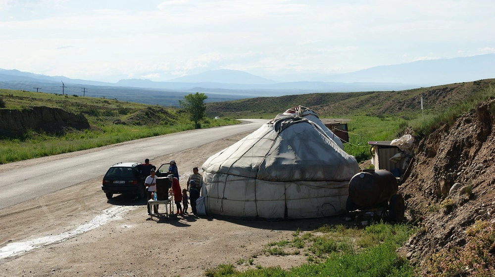 Tradiční jurta u silnice v kyrgyzské krajině s lidmi zastavujícími na krátkou pauzu.