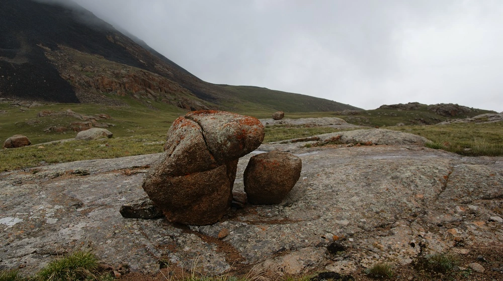 Balvanová formace v horské krajině Kyrgyzstánu pod zataženou oblohou.