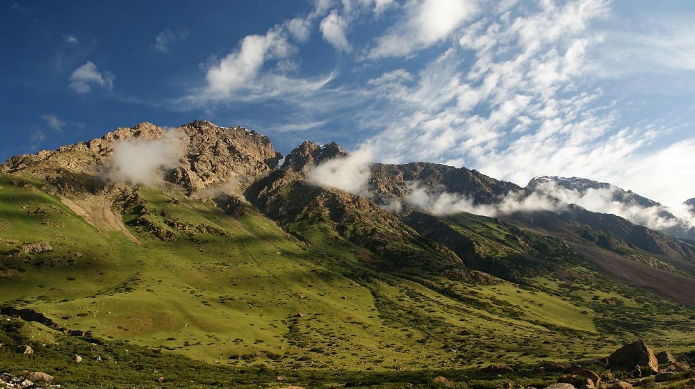 luncem nasvícené zelené svahy a skalnaté hřebeny kyrgyzských hor s nízkými mraky.