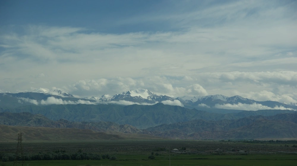Panoramatický pohled na zasněžené hory a údolí v Kyrgyzstánu pod zataženou oblohou.