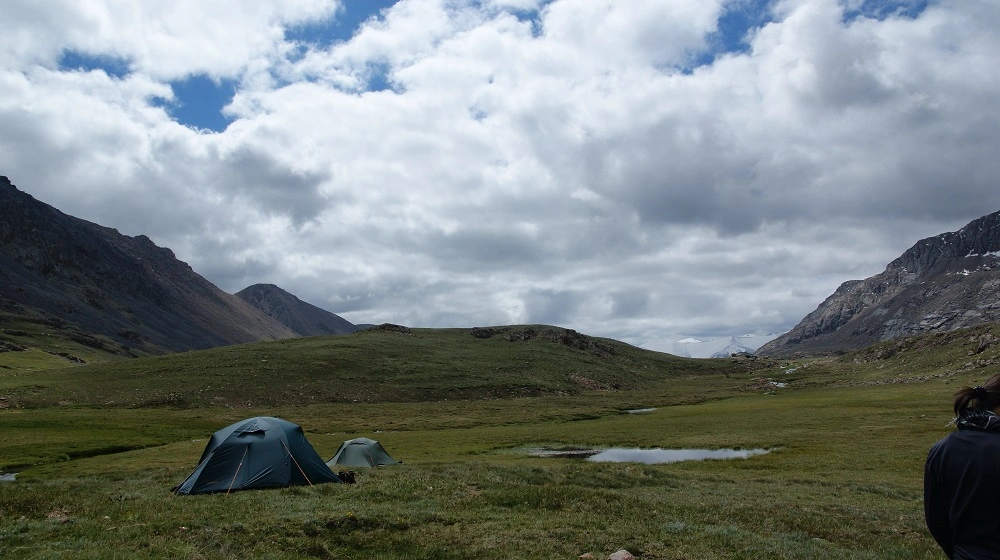 Stany postavené na travnaté planině v kyrgyzských horách pod zataženou oblohou.