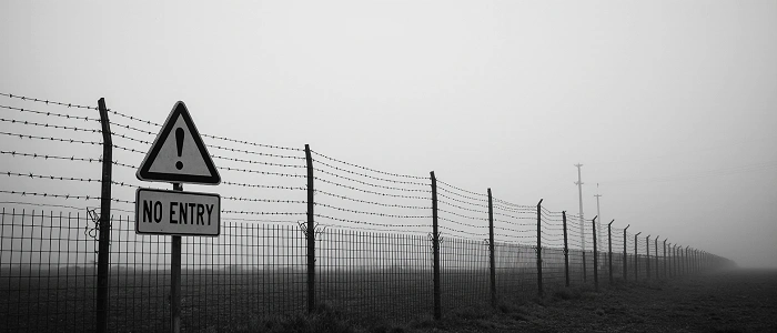 Ostnatý plot se značkou „No Entry“ v mlze, ilustrační foto míst, kam je vstup zakázán a keš sem rozhodně nepatří.