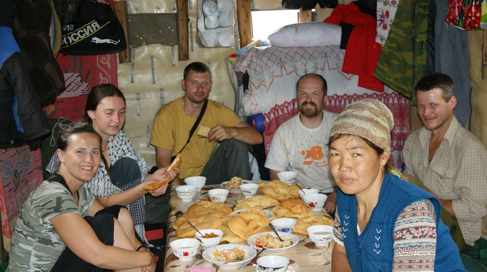 Skupina cestovatelů a místních lidí u společného jídla v tradičním obydlí v Kyrgyzstánu.