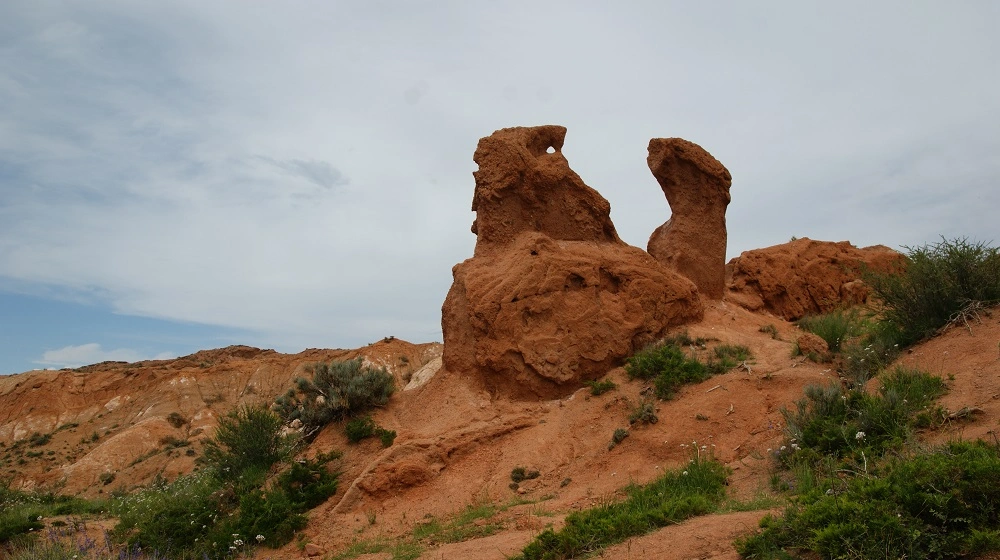 Přírodní skalní útvary z červené zeminy připomínající postavy v krajině Kyrgyzstánu.