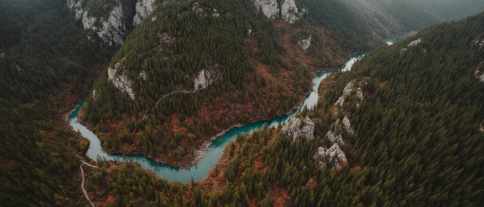 Letecký pohled na říční údolí obklopené lesy a skalami, ilustrační foto k pravidlům geocachingu v přírodě a chráněných územích.
