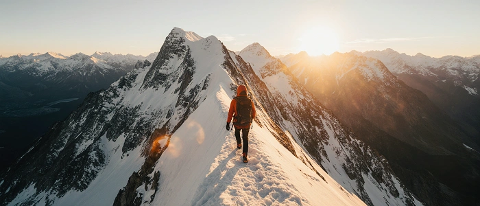 Geokačer kráčí po zasněženém horském hřebeni při východu slunce – symbol výzev a objevování nových extrémů v geocachingu díky funkci Extremes by area.