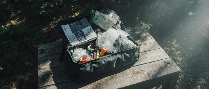 Geocachingová sada na údržbu keší s nářadím, logbooky, páskou a sáčky připravená na opravný výlet v lese.