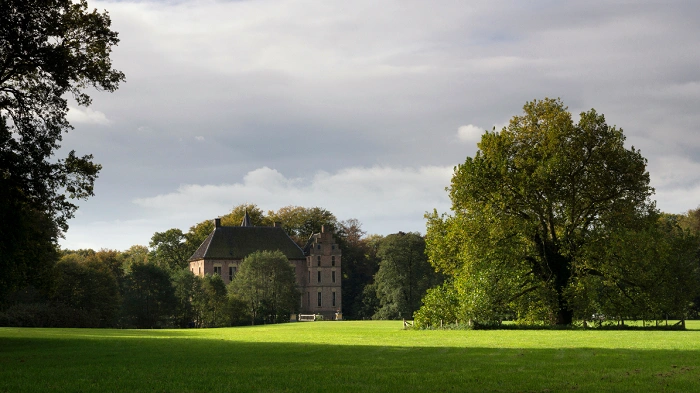 Historický zámecký komplex uprostřed zelené krajiny Bronckhorstu obklopený stromy a rozlehlými loukami.