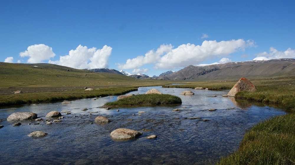 Křišťálově čistá horská řeka v Kyrgyzstánu protékající mezi kameny a pastvinami.