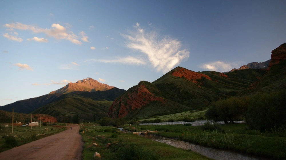Večerní světlo nad zelenými kopci a řekou u vesnice Saruu v Kyrgyzstánu.
