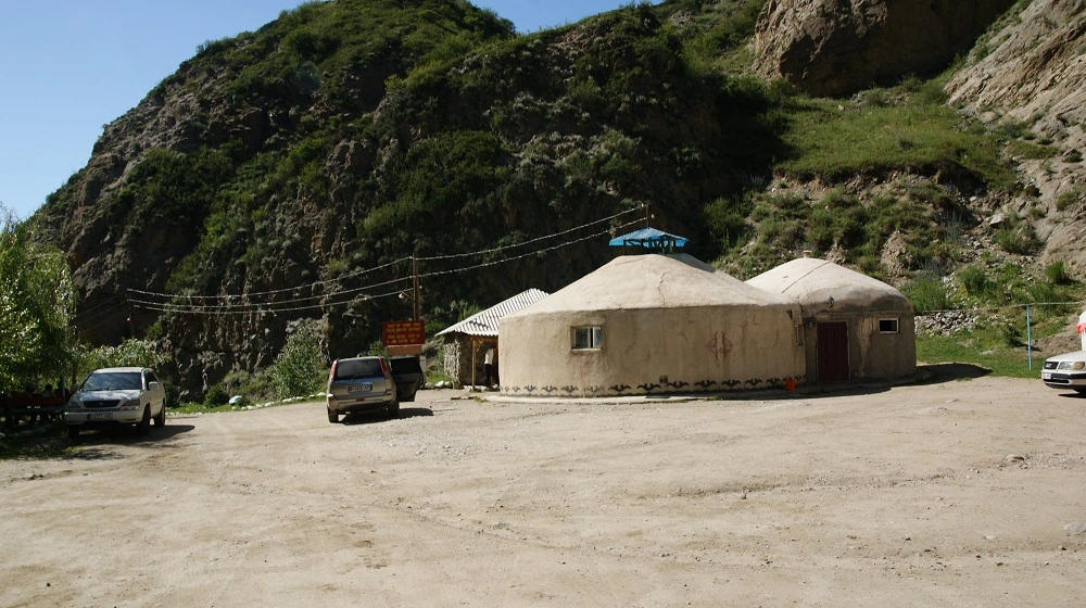 radiční kruhové stavby lázní u skalního masivu v Kyrgyzstánu s parkovištěm před nimi.