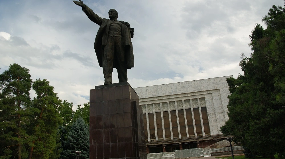 Monumentální socha před kulturní budovou v centru Biškeku obklopená stromy.