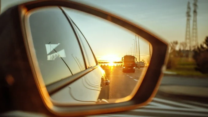 Pohled do zpětného zrcátka auta při západu slunce na cestě za geocachingovým výletem v zahraničí