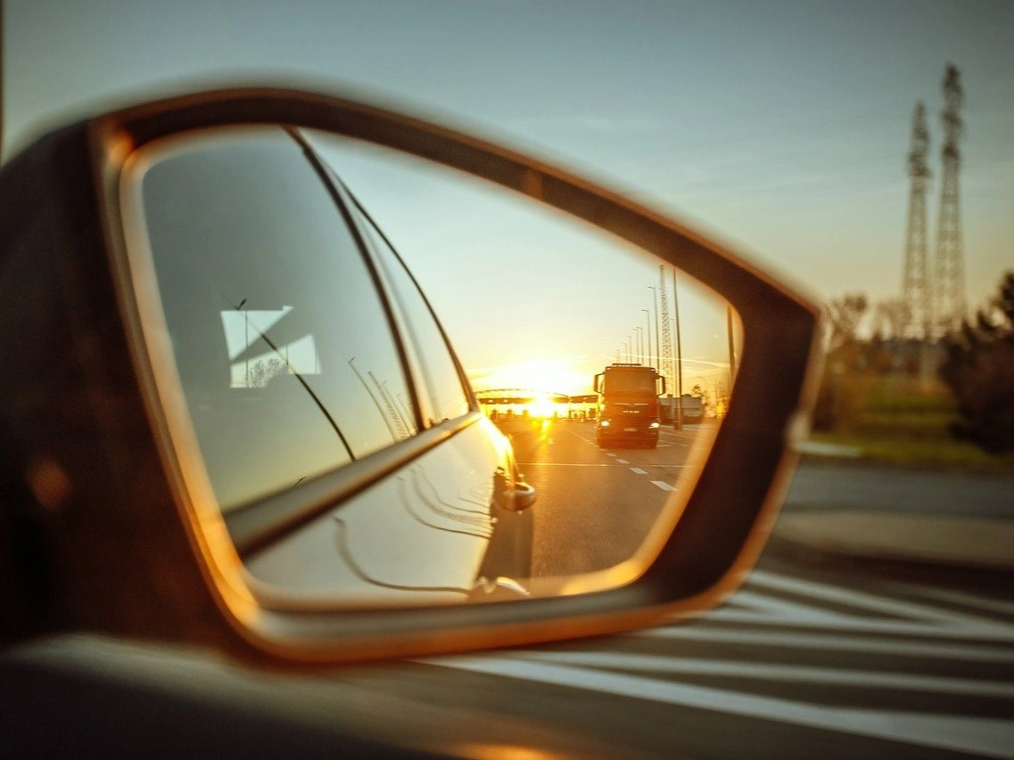 Pohled do zpětného zrcátka auta při západu slunce na cestě za geocachingovým výletem v zahraničí