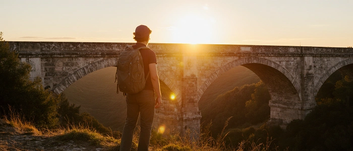 geokačer s batohem u historického mostu při západu slunce