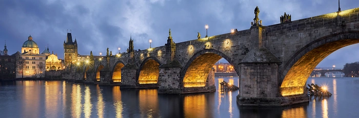 Noční panorama Karlova mostu v Praze s osvětlenými oblouky nad Vltavou.